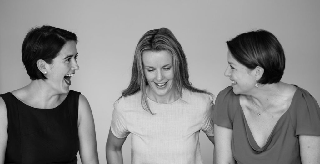 Three women laughing at each other while discussing leadership training